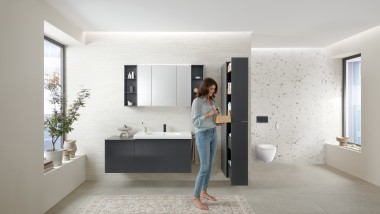 Femme ouvrant une colonne haute avec beaucoup d‘espace de rangement dans une salle de bains avec meubles de salle de bains Geberit Acanto